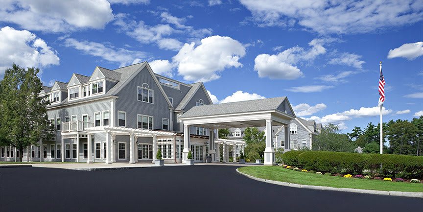 A large residential building with an entrance driveway under a blue sky with clouds.