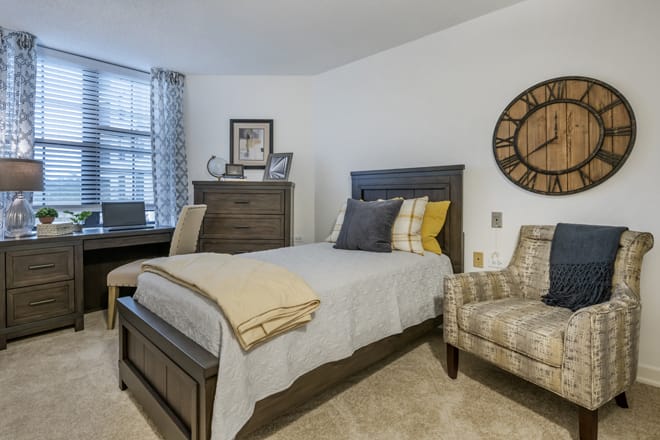 A cozy bedroom with a single bed, decorative pillows, and a wall clock.