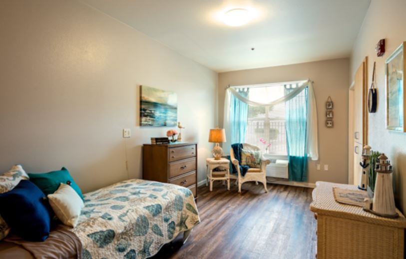 A cozy bedroom with a single bed, wooden flooring, and natural light streaming through the window.