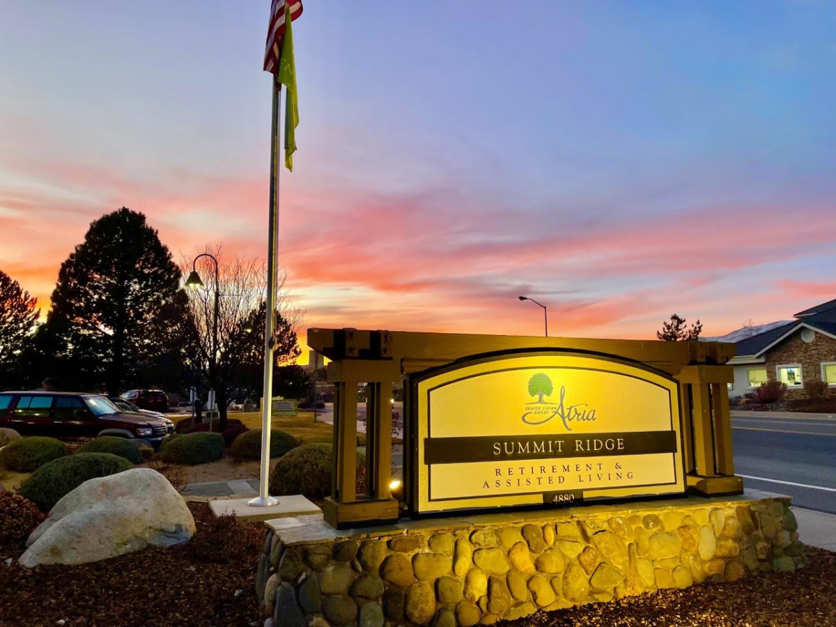 A beautifully lit sign at sunset, with a flag and buildings in the background.