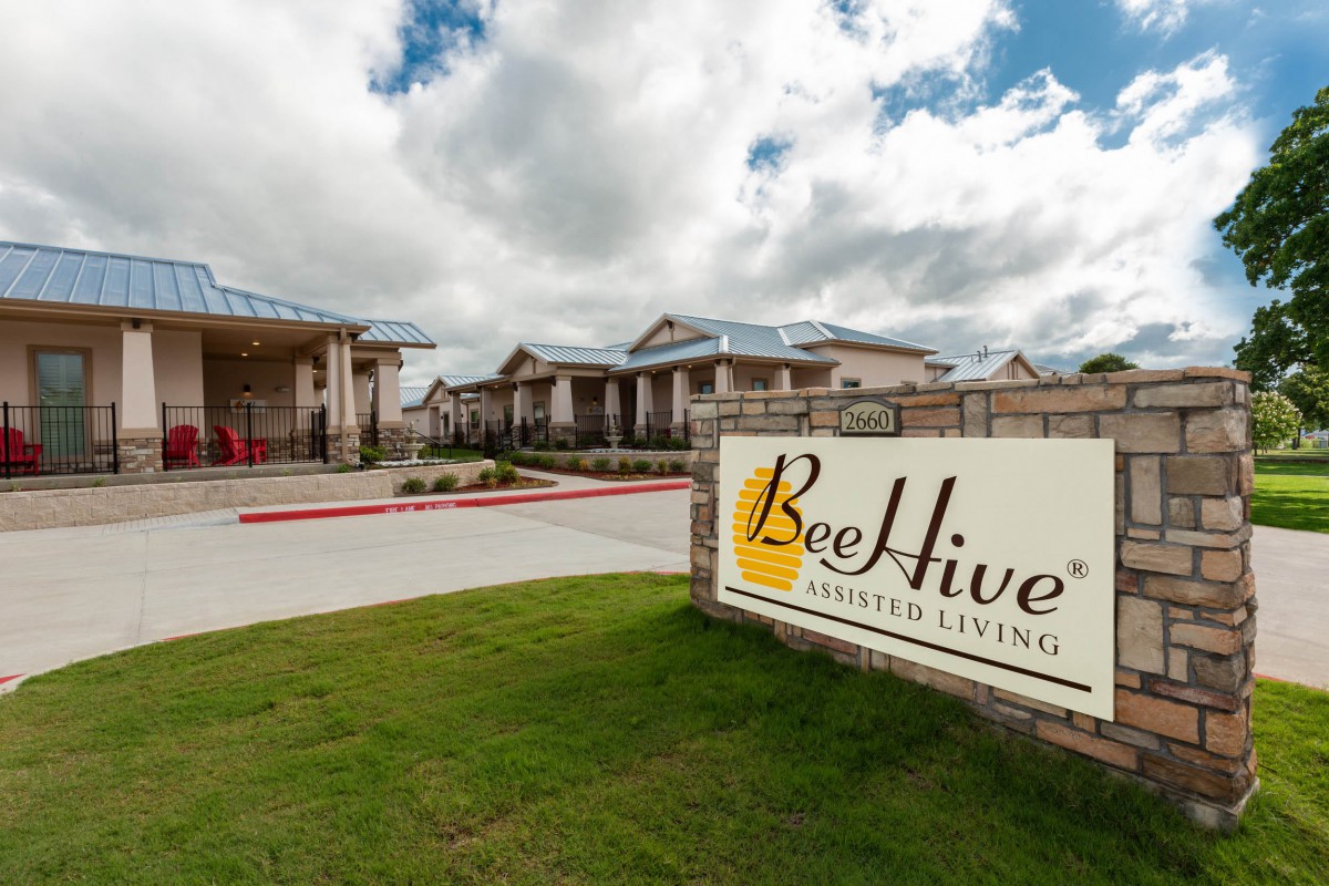 A view of a senior living facility with the BeeHive Homes sign in front, set against a cloudy sky.