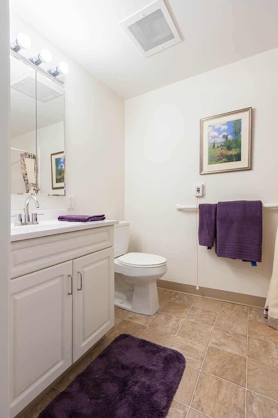 A tidy bathroom with white cabinets and purple towels.