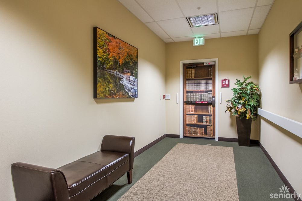 A hallway with a bench, a painting on the wall, and potted plants near a doorway.