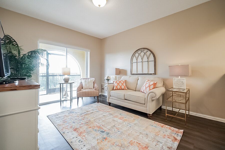 A cozy living room featuring neutral tones with a comfortable sofa, stylish rug, and elegant lamps, opening up to a balcony view.