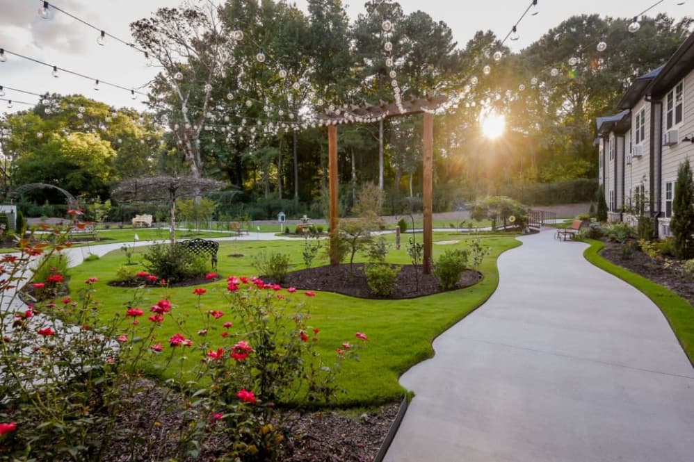 A beautifully landscaped garden at sunset with string lights and vibrant flowers lining a winding pathway.