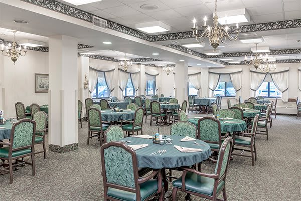 An elegant dining area with multiple tables set for guests, featuring traditional decor and a chandelier.