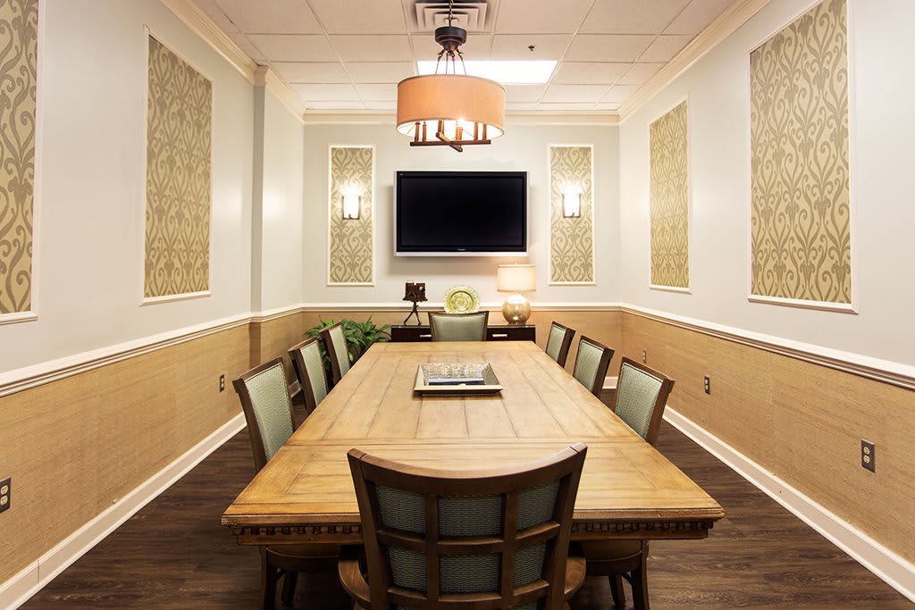 A well-appointed conference room with a large wooden table, cushioned chairs, and a mounted television.