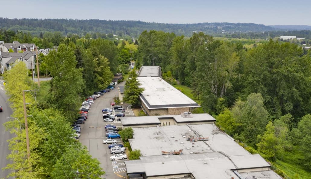 Aerial view of a building surrounded by trees and a parking lot with several cars.