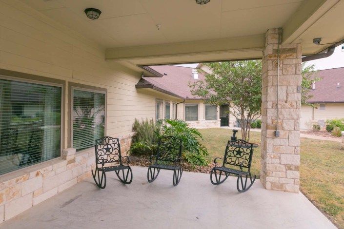 A covered patio area with three decorative metal chairs overlooking a landscaped yard.