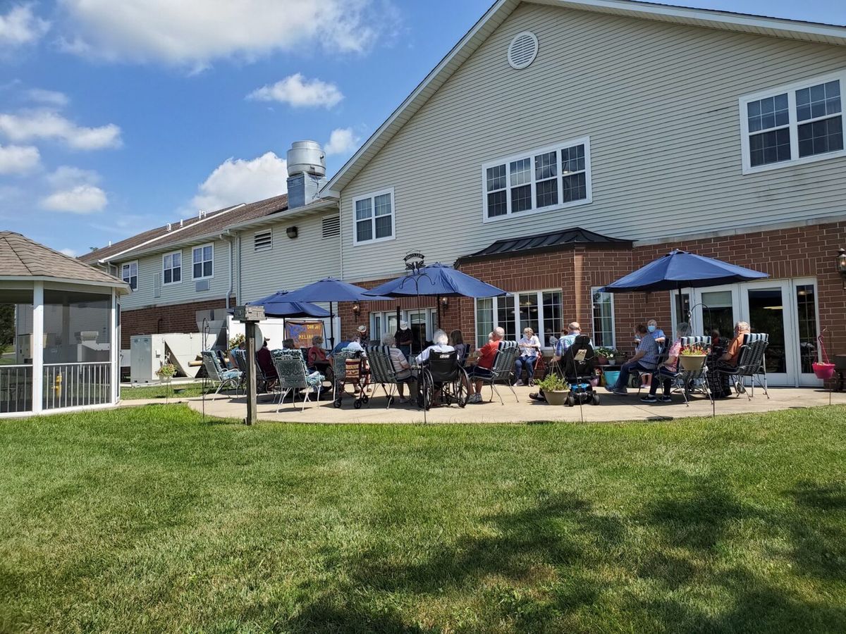 A group of people enjoying a sunny day on a patio with umbrellas outside a large building.