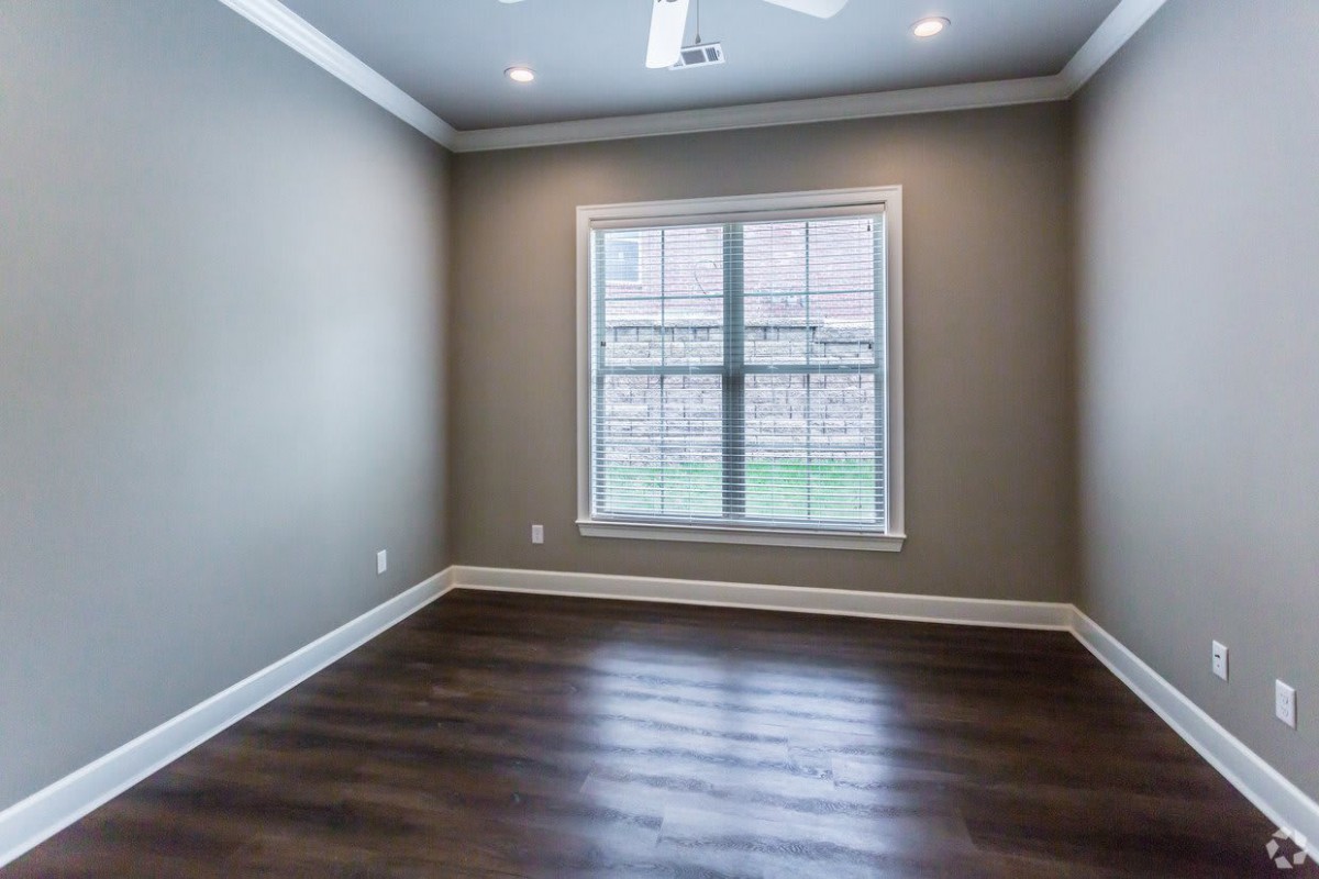 An empty room with hardwood flooring, neutral-colored walls, and a large window allowing natural light to fill the space.