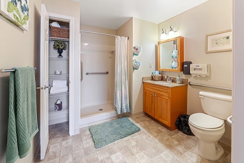 A spacious bathroom featuring a shower, sink with a mirror, and a toilet, complemented by wall-mounted lights and tiled flooring.