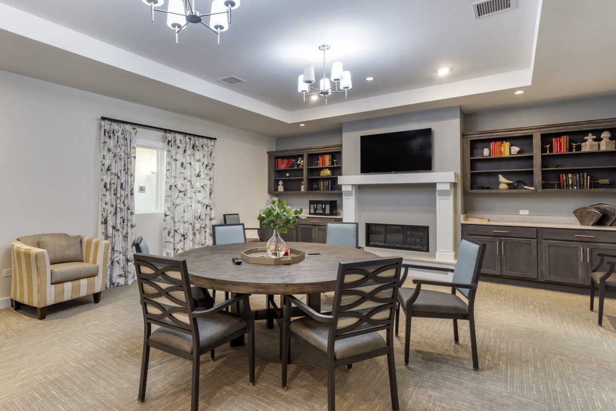 A modern dining room with a round table, chairs, fireplace, and bookshelves.