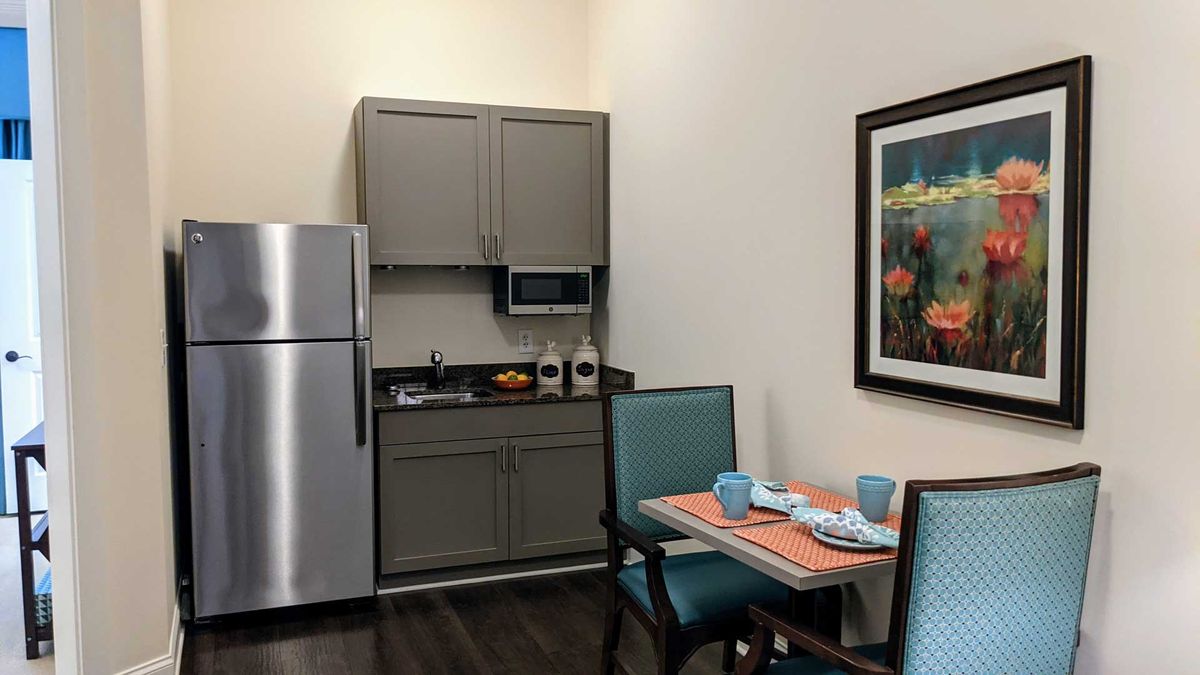 A small kitchen setup with a dining area, featuring a refrigerator, microwave, and neatly arranged tableware.