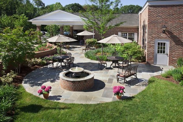 A beautifully landscaped outdoor patio with a central fountain, surrounded by tables and chairs with umbrellas.
