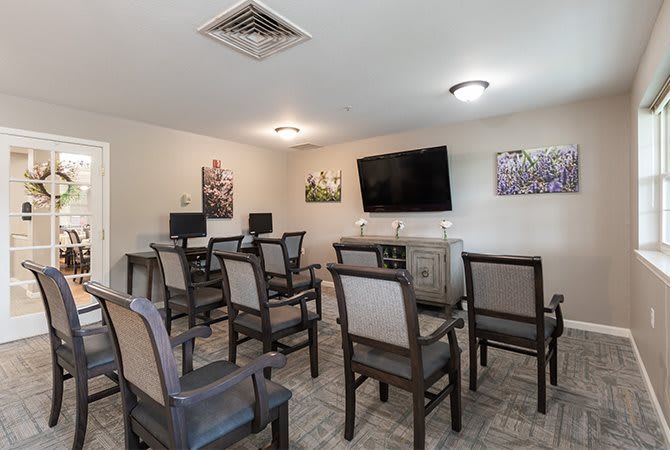 A small conference room with multiple chairs, a television mounted on the wall, and computer stations.