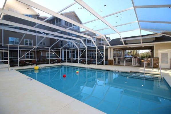 A spacious indoor swimming pool enclosed by a large glass screen, adjacent to a residential building.