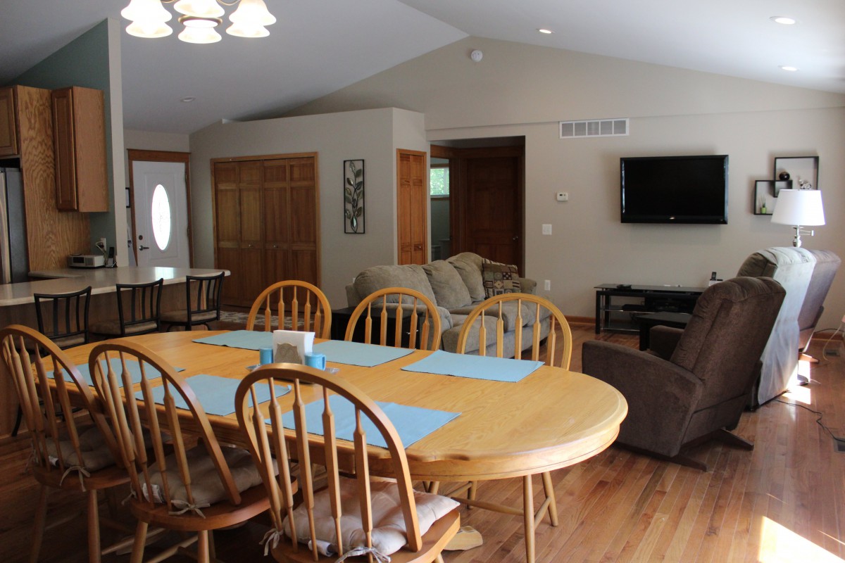 A spacious open-plan dining and living area with a wooden dining table, chairs, and a mounted television.