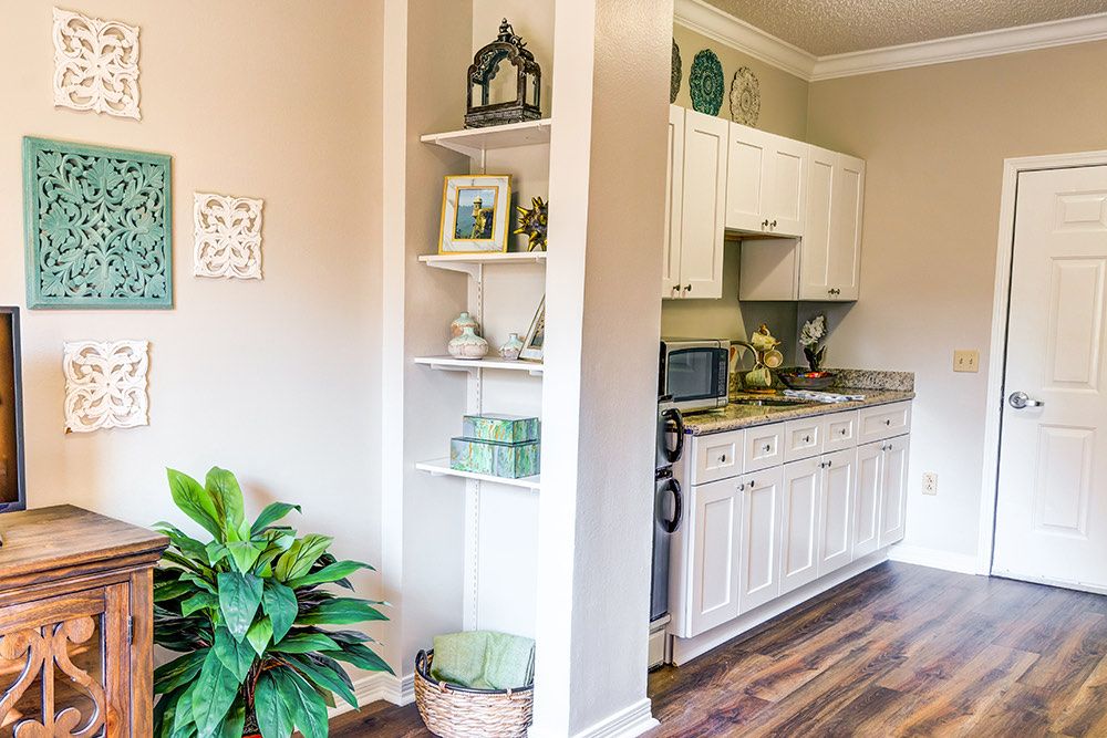 A cozy kitchen corner featuring white cabinets, wooden floors, and decorative shelving with plants.