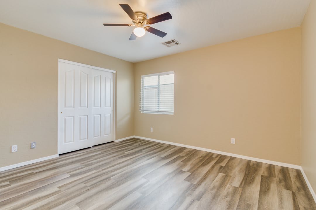 An empty room with laminate flooring and a ceiling fan, featuring a window and closet doors.