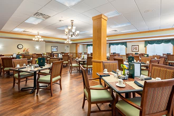 A spacious dining area with neatly arranged tables and chairs, featuring elegant chandeliers and warm wood flooring.