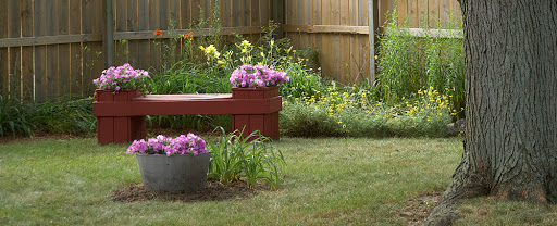A serene garden scene featuring a wooden bench adorned with colorful flowers, surrounded by lush greenery.