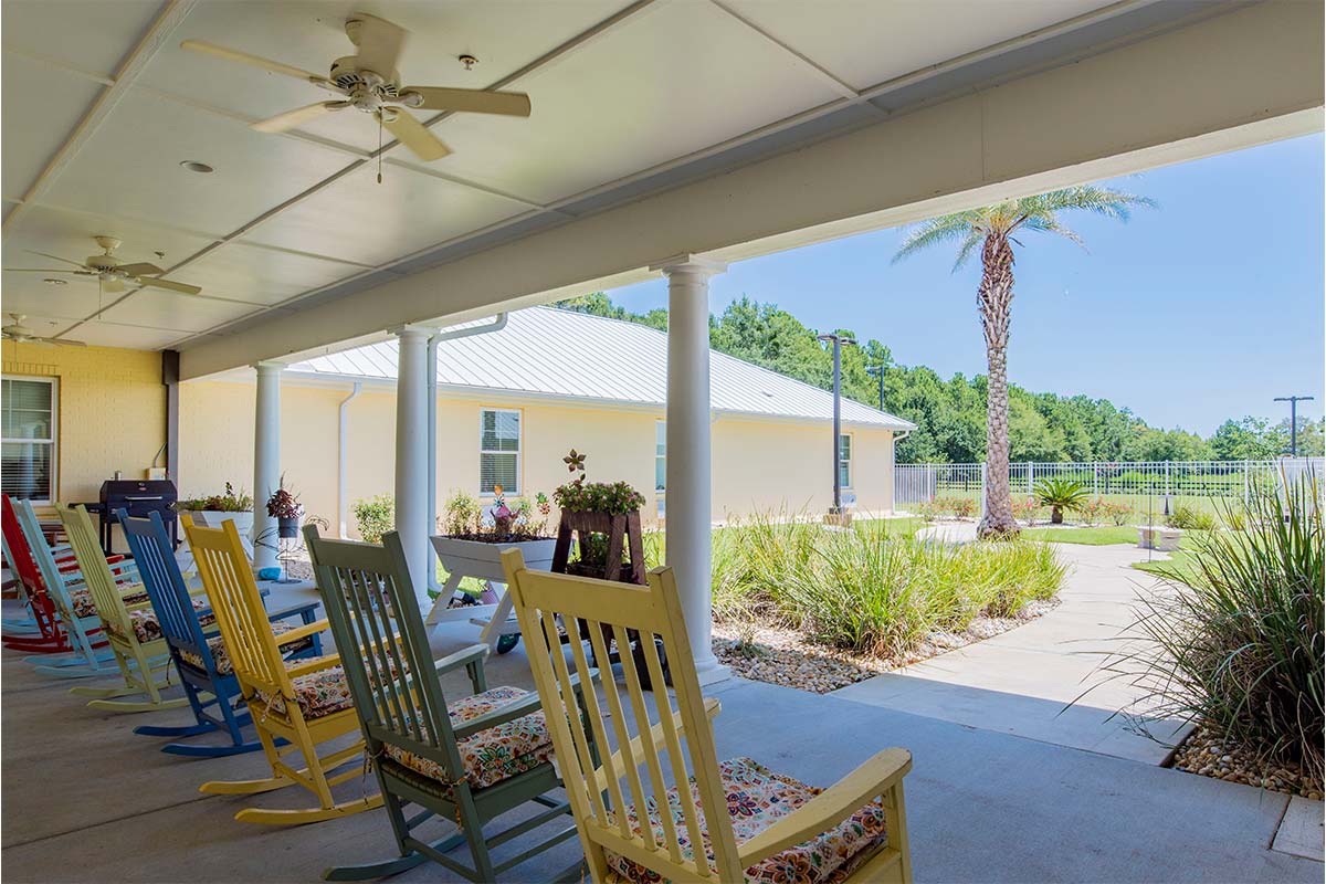 A sunny patio with rocking chairs overlooking a garden and palm tree.
