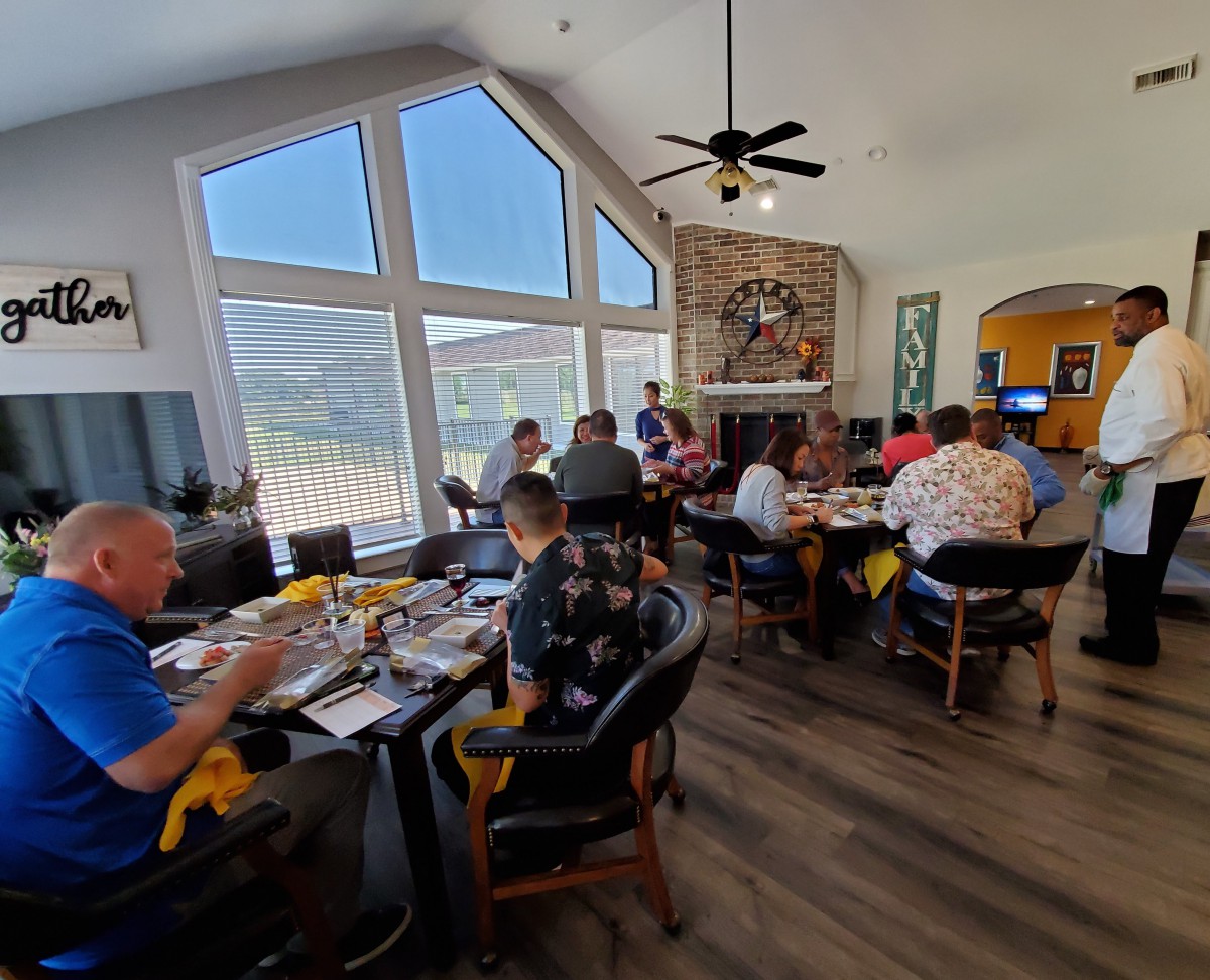 A group of people enjoying a meal together in a well-lit room with large windows.