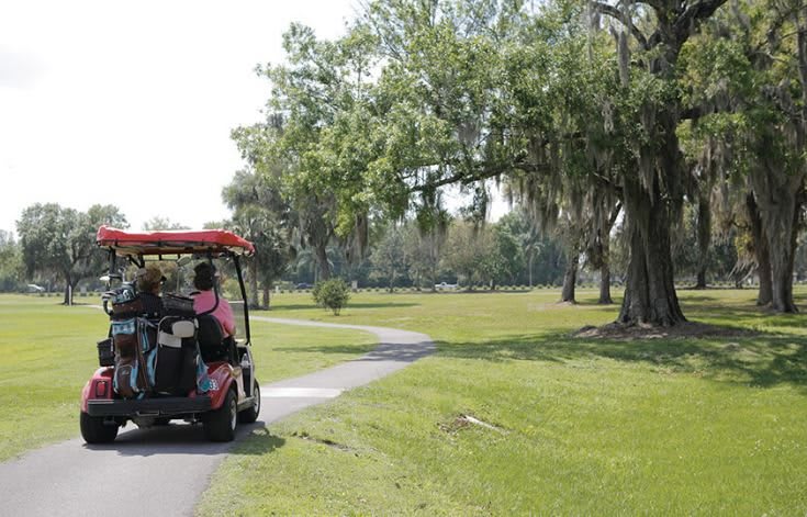A golf cart driving along a scenic pathway surrounded by lush greenery and trees.
