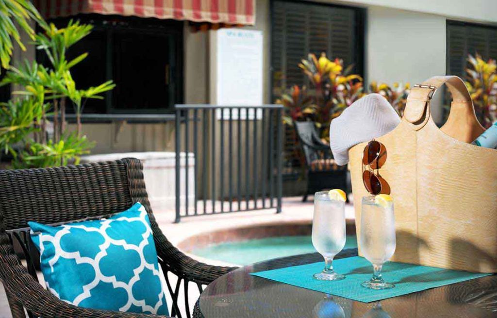 A relaxing poolside setup with iced drinks, sunglasses, and a hat on patio furniture.