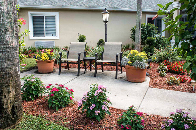 A well-maintained patio with two chairs surrounded by potted plants and colorful flowers.