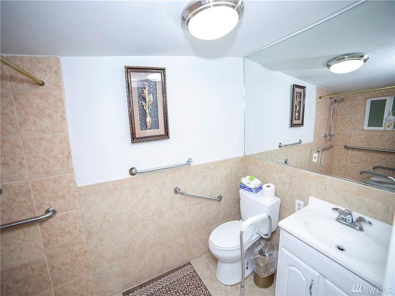 A clean bathroom featuring a toilet, sink, and large mirror with a decorative framed picture on the wall.