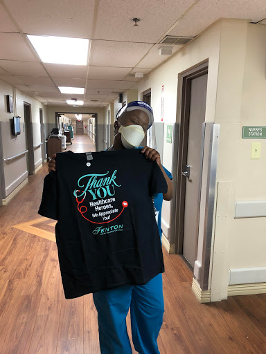 A healthcare worker proudly displays a 'Thank You' shirt in the hospital hallway.