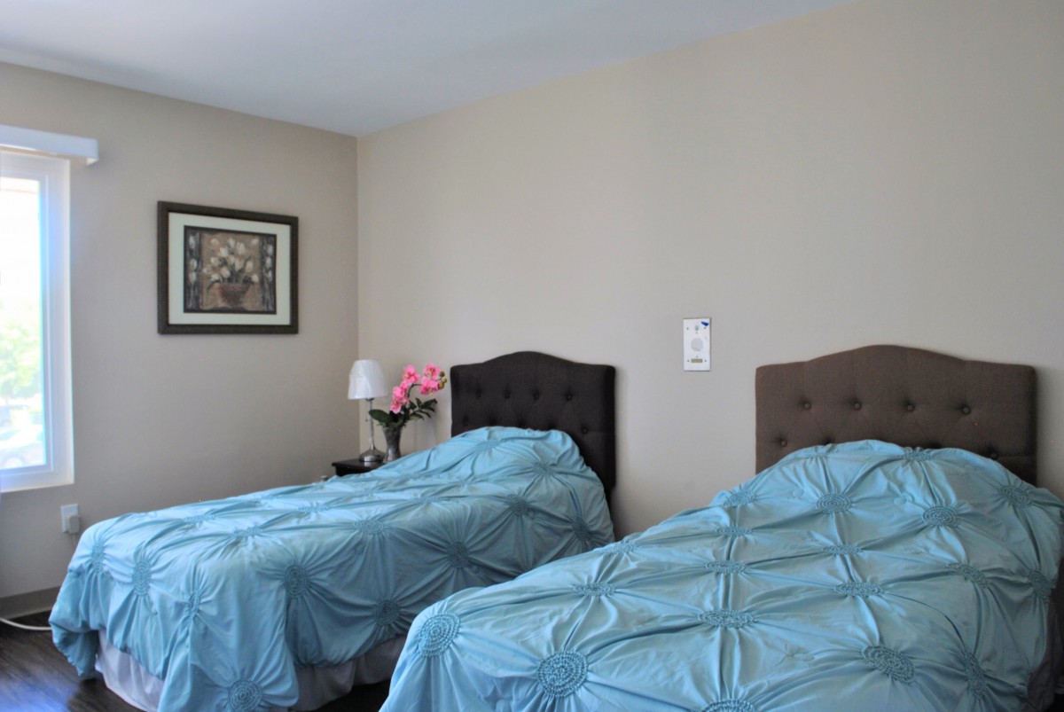 A bedroom featuring two twin beds with blue bedding, a painting on the wall, and a small lamp on a bedside table.