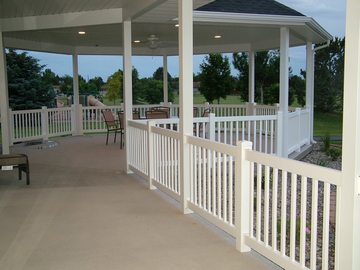 A spacious gazebo with white railings and a view of a lawn.