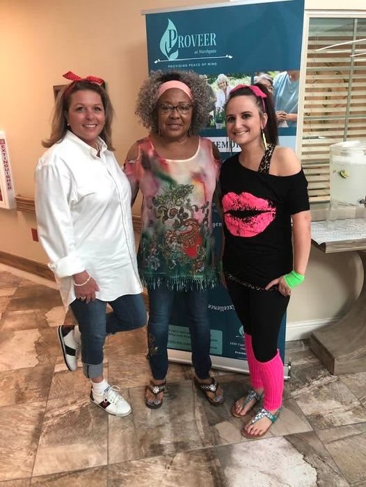 Three women dressed in vibrant 80s-themed outfits pose together at a party.