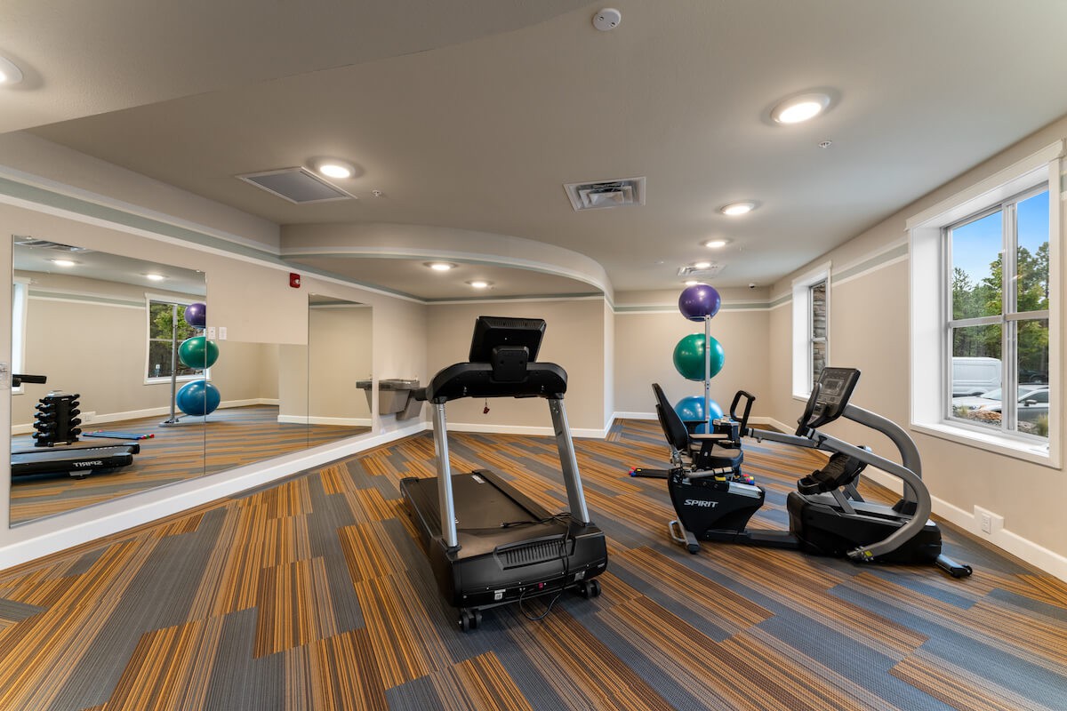 A clean and modern indoor gym featuring a treadmill, exercise bikes, and large mirrors.