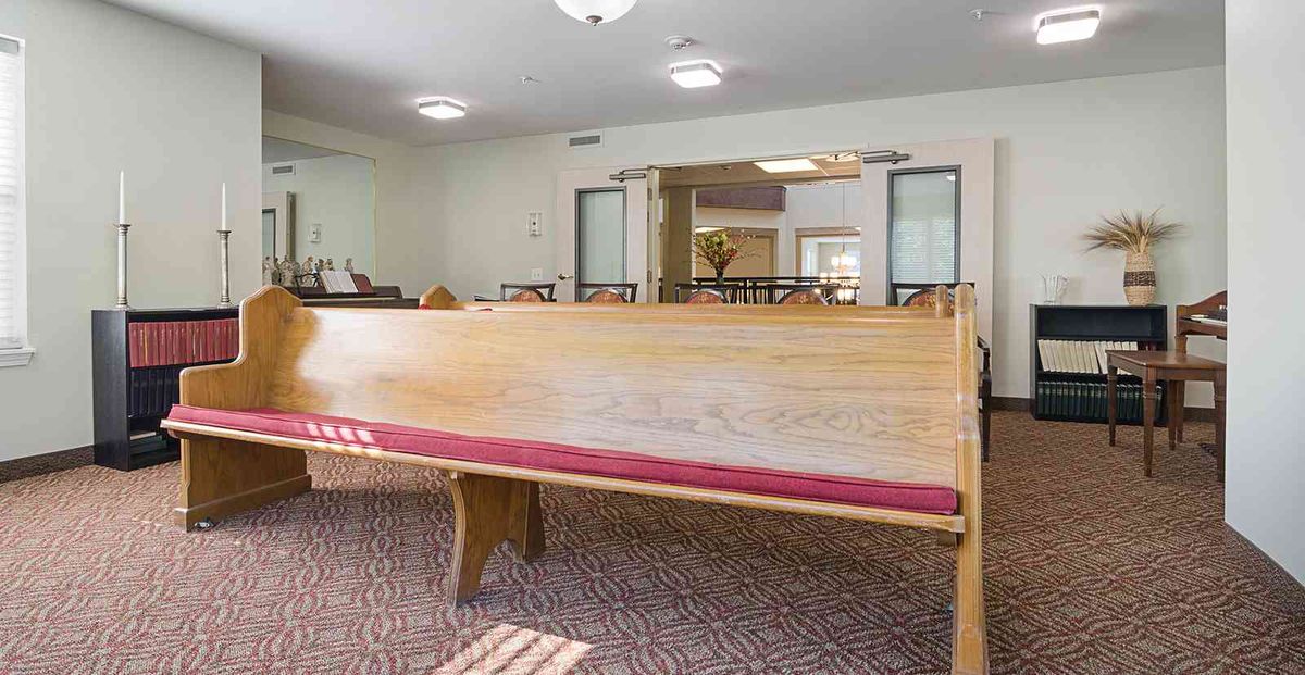 A spacious room featuring a wooden pew with red cushioning.