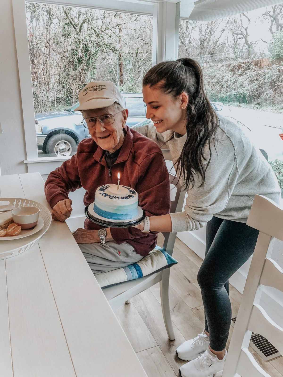 A joyful moment as a young woman presents a birthday cake to an elderly man sitting at the table.