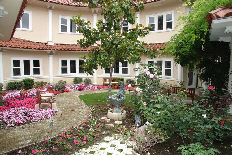 A charming courtyard garden with colorful flowers, a small fountain, and surrounding architecture.
