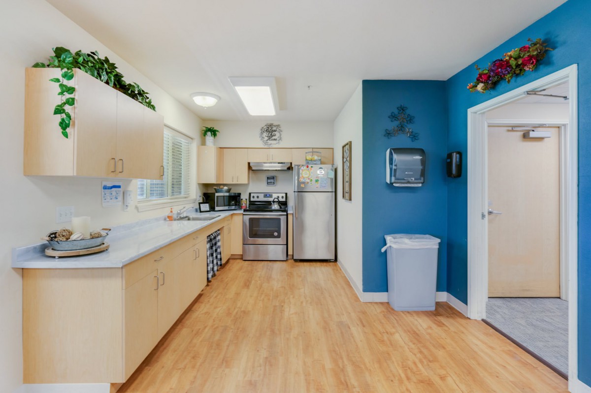 A modern kitchen with wooden flooring and stainless steel appliances, featuring light cabinets and a striking blue accent wall.