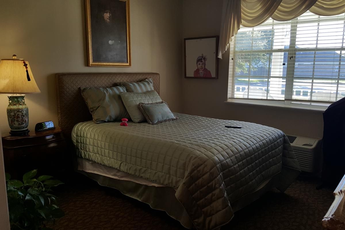 A cozy bedroom with a neatly made bed, adorned with pillows, and sunlight filtering through the window.