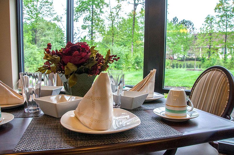 A beautifully set dining table with folded napkins, flower centerpiece, and a scenic window view.