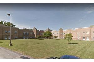 A brick school building with a large lawn and trees under a clear sky.