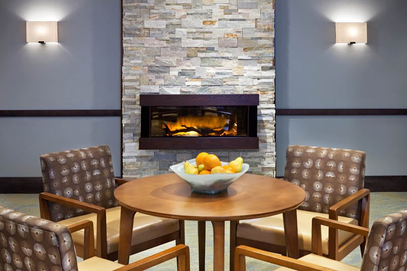 A cozy modern living room with a stone fireplace and a wooden table surrounded by chairs.