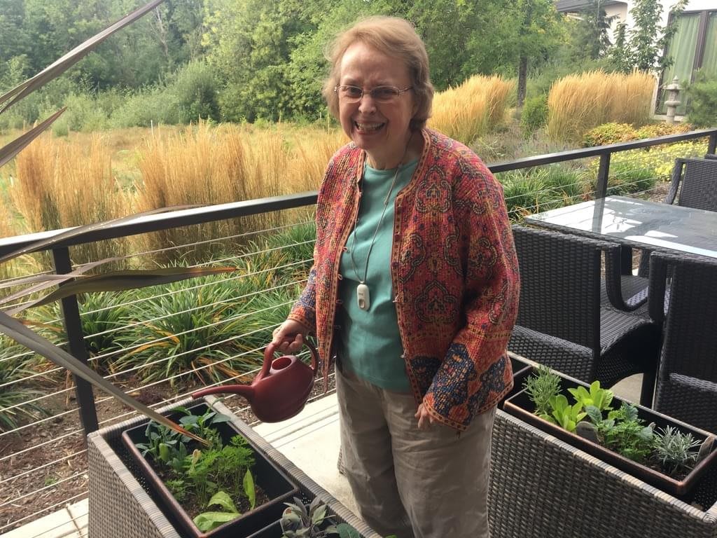 A woman tending to her balcony garden with lush greenery in the background.