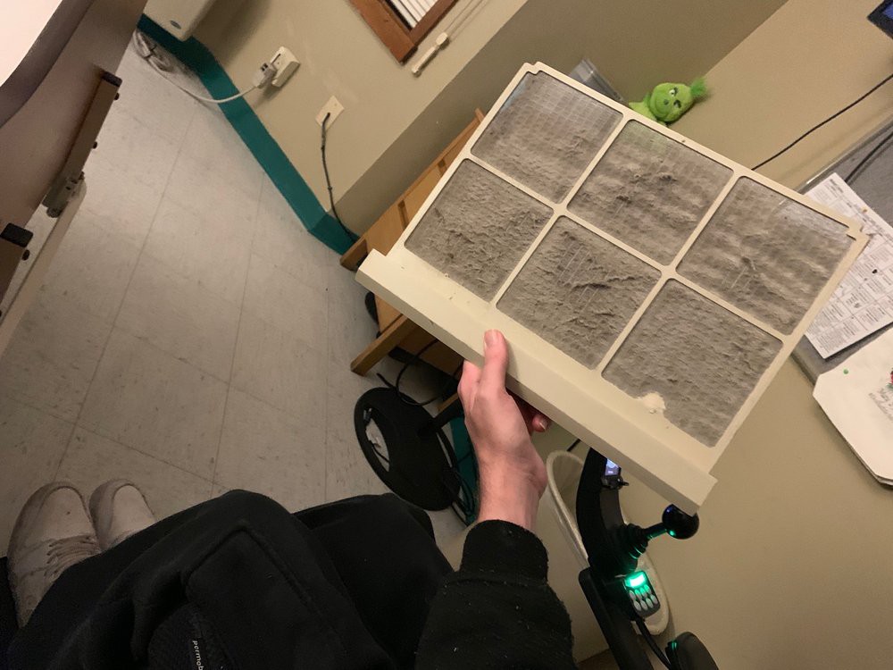 A person holding a dirty air filter in an indoor setting.