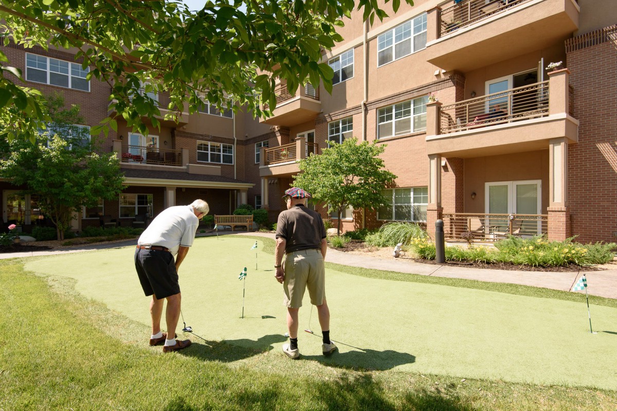 Two men enjoying a game of golf on an outdoor putting green at a retirement community.