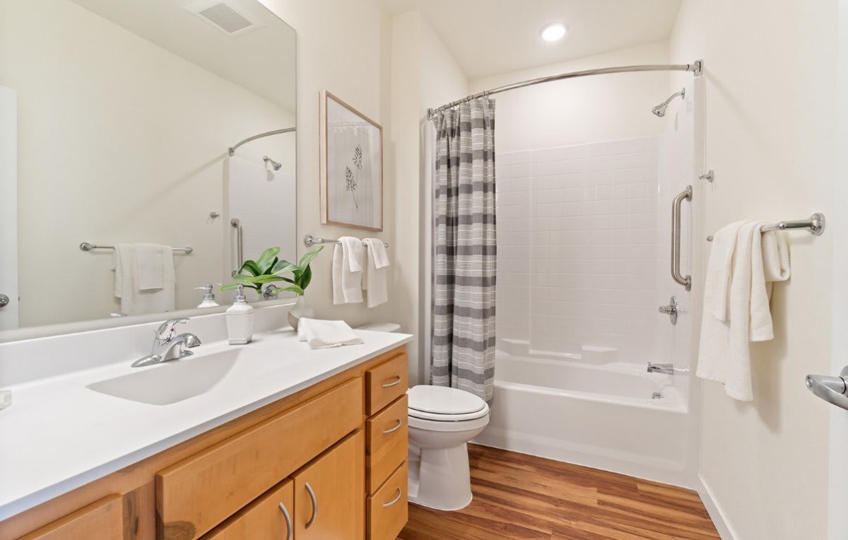 A clean and modern bathroom with wooden flooring, featuring a sink, toilet, and bathtub with a checkered shower curtain.