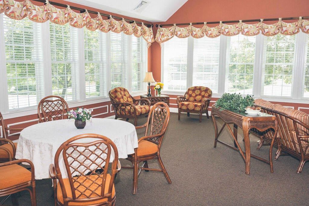 A cozy sunroom with large windows, decorated with wicker furniture and a white tablecloth.